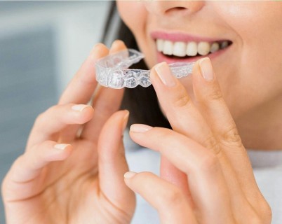 Close-up of a woman smiling and holding a clear dental aligner in her hands.