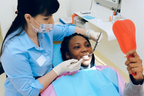 Smiling patient holding a mirror while a dentist in a blue uniform performs a dental checkup.