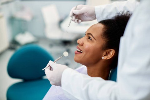 Smiling patient sitting in a dental chair while a dentist examines her teeth with dental tools in a modern clinic.