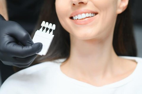 Smiling woman at a dental appointment with a dentist holding a shade guide to match her teeth for whitening or veneers.